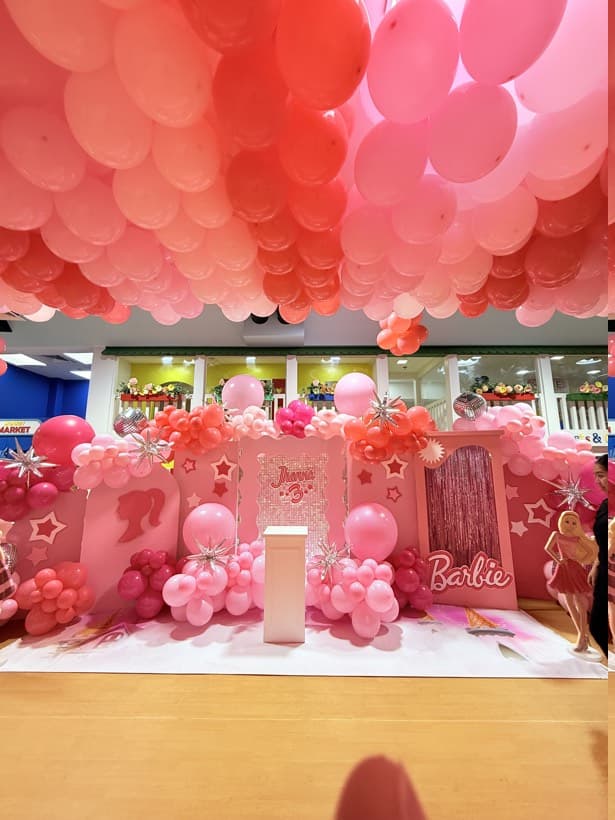 A Barbie party setup with a pink balloon ceiling, star bursts and a sequin backdrop