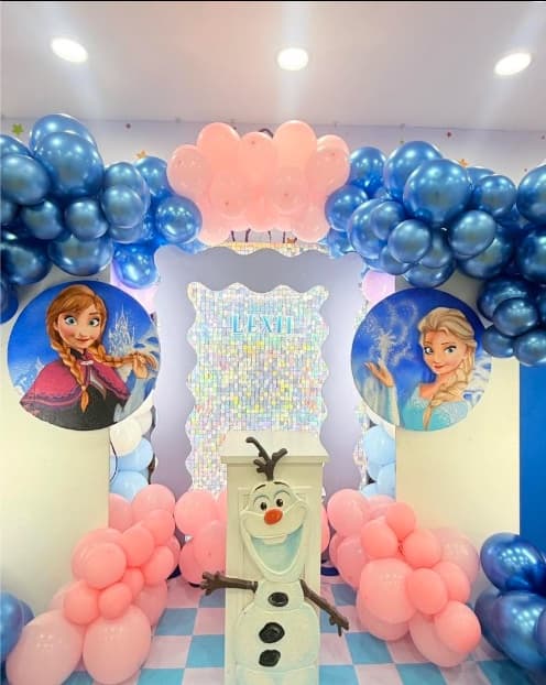A Frozen party setup with blue and pink balloons, Anna, Elsa and Olaf