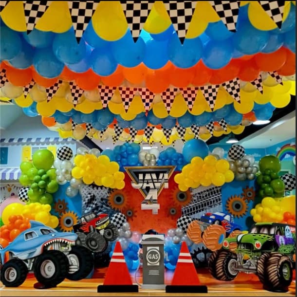 A Monster Jam party setup with a balloon ceiling, checkered bunting and monster trucks