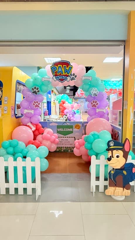 A Paw Patrol party entrance with pastel balloon arches, a picket fence and a Chase cut-out