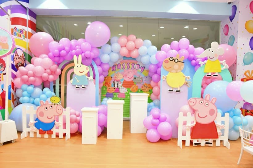 A Peppa Pig party setup with pastel balloons and Peppa, George and family cut-outs