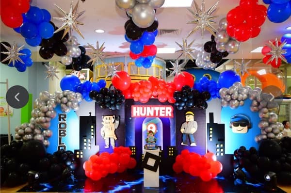 A Roblox party setup with red, blue and silver balloons and a city skyline