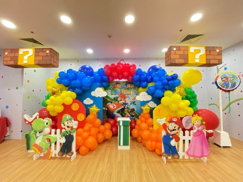 A Super Mario party setup with a balloon arch, question blocks and Mario character cut-outs
