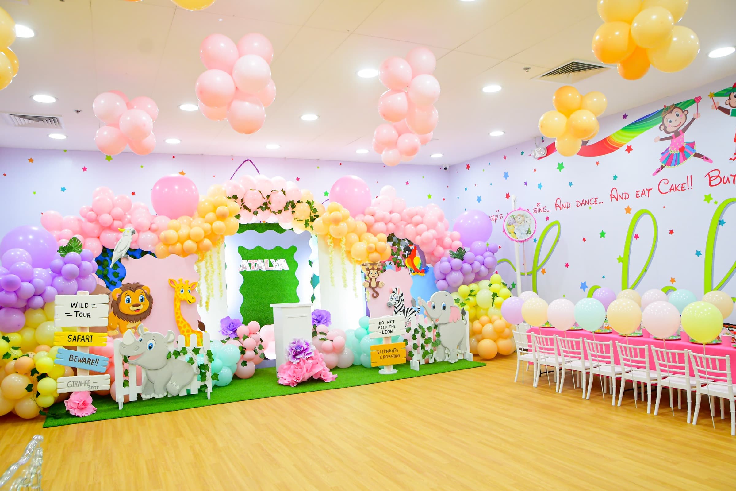A party room dressed in pastel balloons with a garden backdrop and a long kids’ table