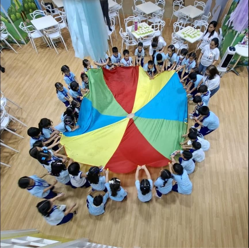 Children in a circle playing a parachute game in the open gym